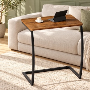 May include: A C-shaped side table with a rectangular brown wood-grain surface and a black metal frame. A white ceramic coffee cup on a saucer and a black tablet computer are placed on the tabletop, which is positioned in front of a sofa.