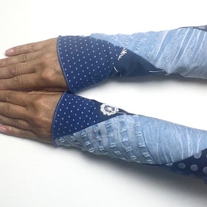 Könnte beinhalten: Armstulpen aus Patchwork-Denim in Blautönen. Die Manschetten sind dunkelblau mit weißen Punkten. Der Körper der Armstulpen hat ein verwaschenes, strukturiertes Aussehen.