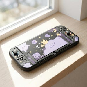 May include: A black handheld gaming console featuring a custom skin with a dark purple night sky theme. The design includes light purple cloud-like characters, yellow stars, a crescent moon, and a small yellow creature with pointed ears.