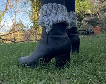 Könnte beinhalten: Schwarze Stiefeletten mit Blockabsatz, getragen mit dunkelgrauen Leggings und grauen Strick-Beinwärmern. Die Stiefel stehen auf grünem Gras im Freien.