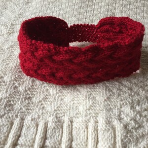 K&ouml;nnte beinhalten: Ein rotes gestricktes Stirnband mit einem geflochtenen Muster.