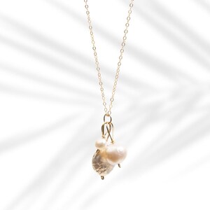 May include: A gold chain necklace with a cluster of three white pearls hanging from it. The pearls are of different sizes and shapes, and the necklace is on a white background.