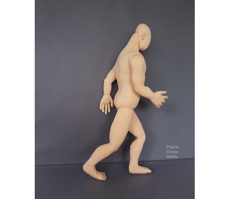 May include: A beige fabric mannequin in a walking pose, with arms outstretched and legs bent. The mannequin is designed to resemble a human figure, with a head, torso, arms, and legs. The background is a solid gray color. The text "Prairie Crocus Studio" is in the lower right corner.