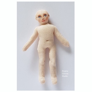 May include: A handmade knitted doll with a painted face, blue eyes, and a light pink complexion. The doll is standing with its arms outstretched.