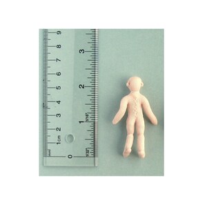 May include: A plain white doll with a simple design, standing on a light blue surface. The doll is about 6 cm tall.