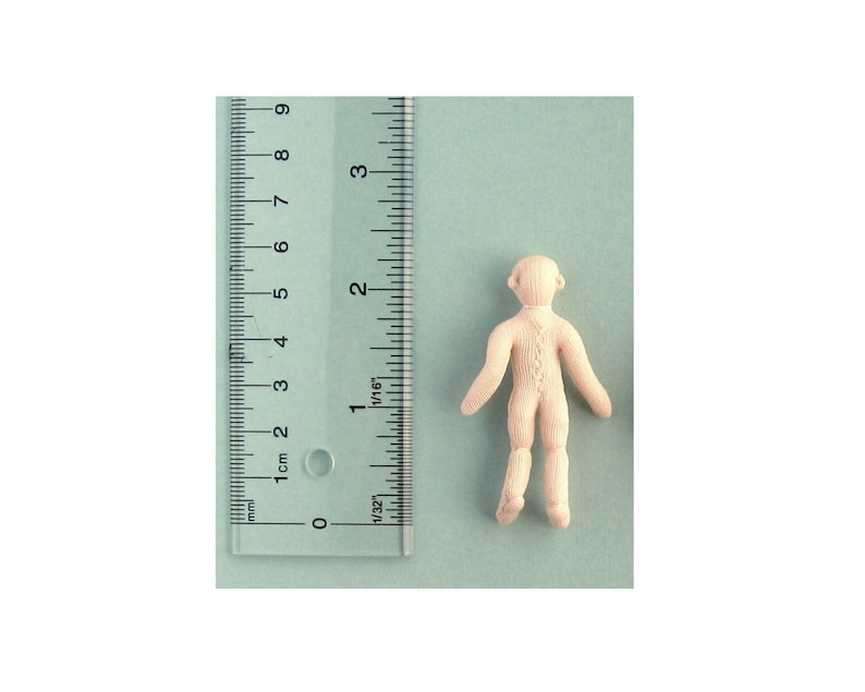 May include: A plain white doll with a simple design, standing on a light blue surface. The doll is about 6 cm tall.