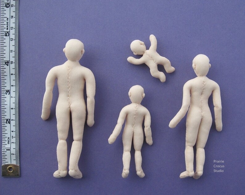 May include: Four handmade fabric dolls of varying sizes, all with a light beige colour. The dolls are standing on a purple surface. The dolls are all in different poses, with one doll lying on its back.