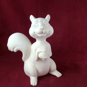 May include: A white ceramic squirrel figurine holding a nut in its paws. The squirrel has a smiling face and a bushy tail.