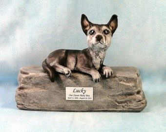 May include: A ceramic dog memorial statue. The dog is gray and brown, lying on a stone-like base. A small plaque on the base reads "Lucky" and includes dates. The statue is a tribute to a beloved pet.