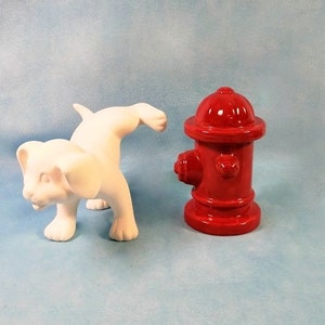 May include: A white ceramic lion cub figurine and a red fire hydrant. The lion cub is in a playful pose, and the fire hydrant is a classic design. The objects are set against a light blue background.