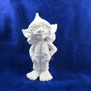 Peut inclure: Figurine de gnome en céramique blanche, souriant, portant un chapeau pointu, une veste et un pantalon. Le gnome a des cheveux bouclés et se tient avec une main sur la hanche. Fond bleu.