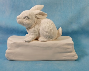 May include: A white ceramic figurine of a small rabbit sitting on a rectangular base. The rabbit has detailed fur texture, pointed ears, and a small tail. The entire piece is unpainted, matte white, and features a smooth, solid construction.
