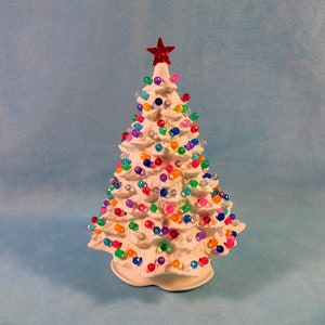 May include: A ceramic Christmas tree with a white finish, adorned with colorful, round lights. A red star tops the tree. The tree is a festive holiday decoration.