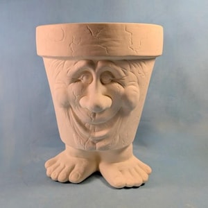 May include: A matte off-white ceramic planter shaped like a pot with a sculpted face and two feet at the base. The surface features a textured, cracked appearance across the rim and the facial features, including a nose, eyes, and a wide mouth.