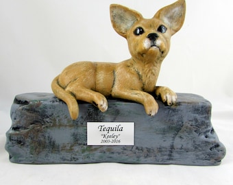 May include: A ceramic figurine of a tan chihuahua dog lying on a gray and green rock base. The base has a small silver plaque with the text "Tequila "Keeley" 2003-2016".