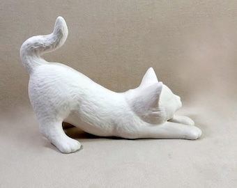 May include: A white ceramic cat figurine in a playful pose, with its tail curled around its body and its head turned to the side. The figurine is unpainted and ready to be decorated.