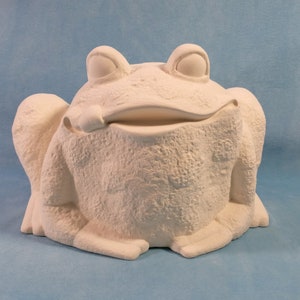 May include: White ceramic frog figurine with a wide, open mouth and large, round eyes. The frog is sitting on its bottom with its legs tucked in.