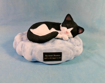 May include: A black and white cat figurine sleeping on a blue cloud-shaped base. The base has a small plaque with the text "My sweet Moomoo April 12, 2013 - August 12, 2019".
