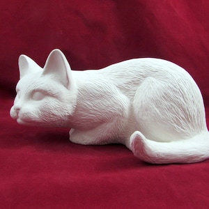 Peut inclure: Figurine de chat en céramique blanche en position de repos. Le chat est couché, la tête et la queue légèrement relevées. La figurine présente une texture de fourrure détaillée, sur fond rouge foncé.