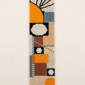 Può includere: Una striscia rettangolare di perline con un motivo geometrico in arancione, marrone, grigio, beige, nero e bianco. Il design include forme circolari, blocchi solidi e linee sottili. Il testo CLAROSA7 è stampato in nero nella parte inferiore.
