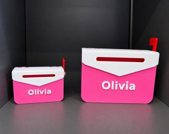 May include: Two pink and white mailboxes of different sizes, each featuring a white top flap with a horizontal slot and a small red flag on the side. The name Olivia is printed in white capital letters on the front of both mailboxes.