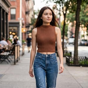 Puede incluir: Una camiseta sin mangas de punto acanalado marrón con cuello alto combinada con pantalones vaqueros azules. La parte superior presenta una silueta ajustada y una textura acanalada vertical, mientras que los vaqueros tienen un lavado azul clásico.