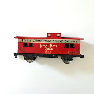 May include: A red toy train caboose with the text "Nickel Plate High Speed Service" and "Nickel Plate Road 956". The caboose has black wheels and a silver stripe.
