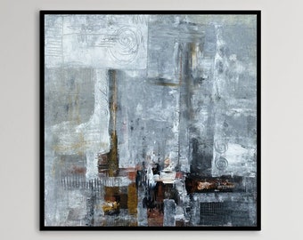 May include: A gray and white abstract painting with brown and black accents hangs above a light gray sofa with two white pillows. The painting is in a black frame and is centered on the wall. The sofa is in a living room setting with a wooden floor and a white wall.