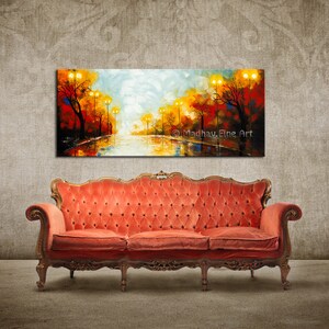 May include: A colorful abstract painting of a street scene with trees and streetlights. The painting is hanging on a wall above a red velvet sofa.