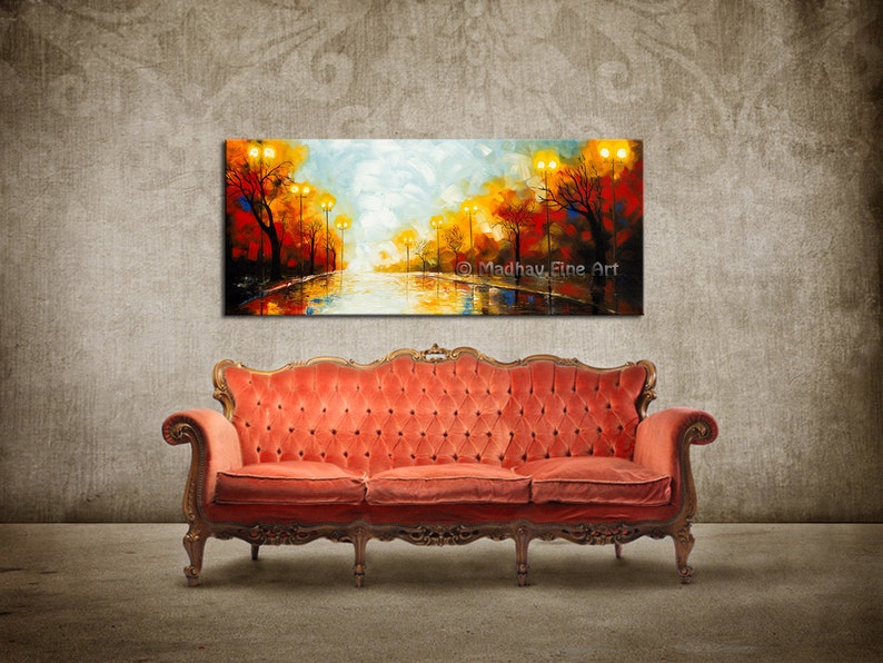 May include: A colorful abstract painting of a street scene with trees and streetlights. The painting is hanging on a wall above a red velvet sofa.