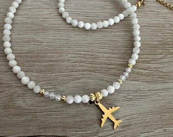 May include: White beaded necklace and bracelet set with a gold-colored airplane charm. The necklace and bracelet are made of small, round, white beads. The airplane charm is suspended from the necklace.