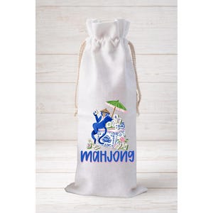 May include: White drawstring wine bag featuring a blue cartoon monkey holding a green umbrella and playing Mahjong. The bag has a beige drawstring and the word "Mahjong" in blue script.