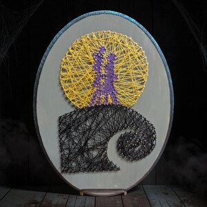 May include: An oval string art piece on a gray wooden board featuring a large yellow circular moon, two purple figures standing together, and a black swirling hill base created with nails and thread in a layered, geometric design.