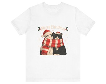 Peut inclure: Un t-shirt blanc à manches courtes avec une illustration de deux chats portant des bonnets de Noël rouges et blancs, enveloppés dans une écharpe rayée rouge et blanche. Le texte Merry Christmas est inscrit au-dessus des chats.