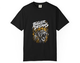 Könnte beinhalten: Ein schwarzes Kurzarm-T-Shirt mit einem Grafikdruck eines brüllenden Löwen, der eine goldene Krone trägt. Über dem Löwen steht der Text BIGGER DREAMS in weißen Buchstaben. Das Design enthält gelbe und weiße Farbspritzer-Akzente.