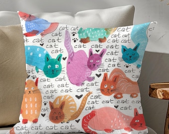 May include: A white throw pillow with a colorful pattern of cats. The cats are drawn in a whimsical style and are surrounded by the word "cat" repeated many times.