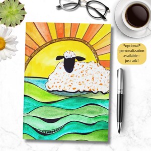 Può includere: Un taccuino colorato con un'illustrazione di pecora, un sole e colline. La pecora è bianca con la faccia nera, su un sole giallo e arancione. Il testo "*optional* personalization available-- just ask!" è in un riquadro giallo.