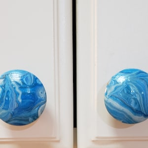 May include: Two blue and white marbled cabinet knobs. The knobs are round and have a glossy finish.