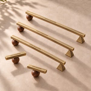 May include: A set of five cabinet pulls and knobs featuring a brushed brass rectangular bar and a dark brown spherical wooden base. Each piece is engraved with the text vxtttvdqekOffc on the top surface of the brass bar.