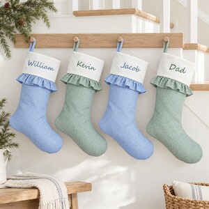 May include: Four fabric Christmas stockings with a gingham pattern in blue and green. Each stocking features a white cuff with a ruffled edge and a personalized name embroidered in blue or green thread: William, Kevin, Jacob, and Dad.