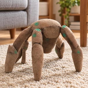 May include: A brown plush toy shaped like a multi-legged creature with a rounded body and segmented limbs. The fabric features a textured appearance with scattered, small, bright green spots across the surface of the head and legs.
