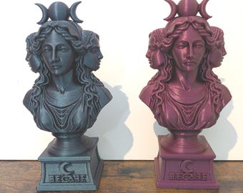 May include: Two busts of a woman with multiple faces and a crescent moon crown. One is a dark teal color, the other is a deep magenta. Each bust sits on a rectangular base with the word "HECATE" and a crescent moon symbol.