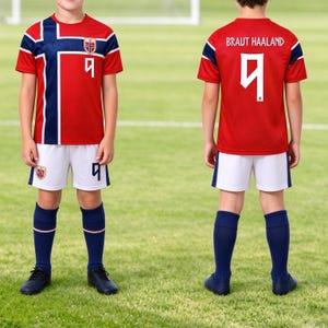May include: A red soccer jersey with a blue and white cross pattern, the number 9, and the Norway flag emblem. The back displays the name BRAUT HAALAND and the number 9. The set includes white shorts with the number 9 and navy blue soccer socks.