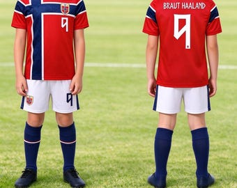 May include: A red soccer jersey with a blue and white cross pattern, the number 9, and the Norway flag emblem. The back displays the name BRAUT HAALAND and the number 9. The set includes white shorts with the number 9 and navy blue soccer socks.