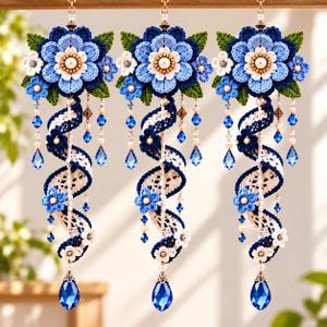 May include: Three hanging ornaments featuring crocheted blue and white flowers with green leaves. Each piece includes a spiraling lace ribbon, dangling pearl beads, and small blue crystals, finished with a large teardrop-shaped blue crystal pendant.