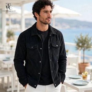 May include: A black corduroy jacket featuring a classic collar, long sleeves, and two chest pockets with button closures. The jacket has a front button-down placket with matching black buttons and is worn over a plain black t-shirt and white trousers.