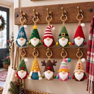 May include: Ten crocheted gnome keychains hanging on a wooden rack. Each gnome features a white beard, a round nose, and a unique hat design, including patterns like snowflakes, stripes, reindeer antlers, and holiday-themed colors like red, green, and gold.