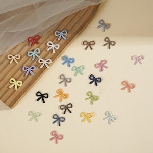 May include: A collection of small, multi-colored velvet ribbon bows in various shades including red, blue, white, yellow, pink, green, black, and brown. These decorative bow embellishments are scattered across a wooden board and a plain surface.