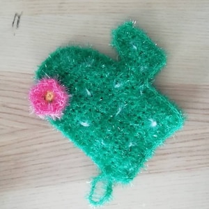 Peut inclure: Un cactus crocheté vert avec une fleur rose. Le cactus a la forme d'une main avec un doigt pointé vers le haut.