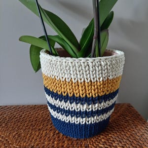 Peut inclure: Un cache-pot en crochet rayé blanc, jaune et bleu. Le cache-pot est fait de fil épais et a un motif texturé.